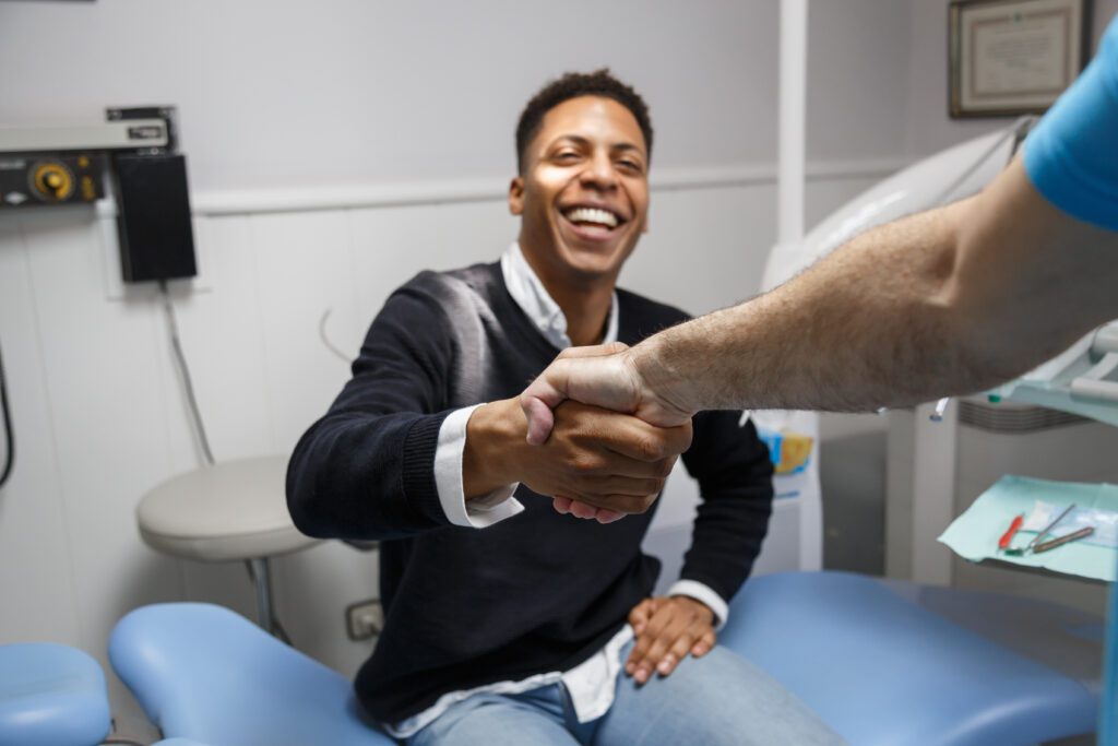 Young African-American man shaking hand of crop dentist having v